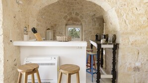 A kitchen with stone walls, a white countertop, and wooden stools.