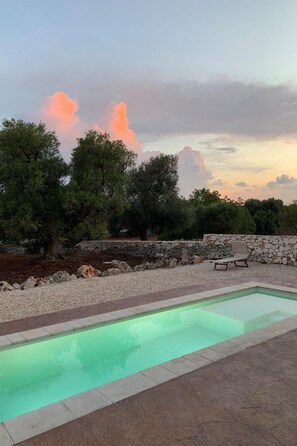 A swimming pool with a stone wall and a lounge chair.