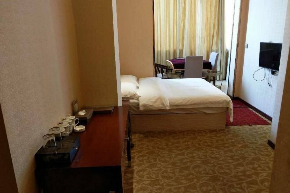 A hotel room with a bed, a desk, a chair, a TV, and a window with curtains.