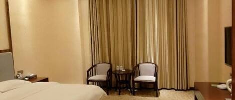 Ein Hotelzimmer mit einem großen Bett, zwei Sesseln, einem kleinen Tisch und einem Fernseher.