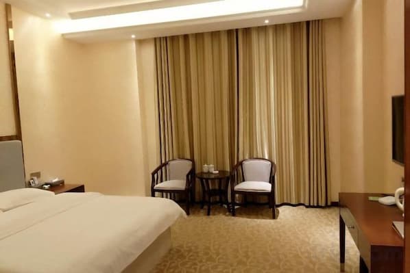 Una habitación de hotel con una cama grande, dos sillas, una mesita y un televisor.