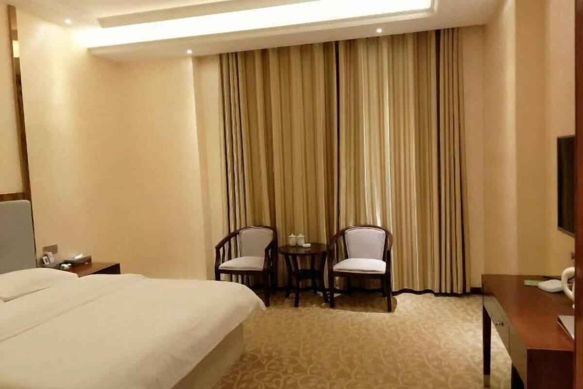 A hotel room with a large bed, two chairs, a small table, and a TV.