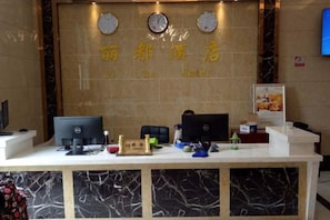 Un mostrador de recepción de hotel con encimera de mármol, dos monitores, una caja registradora y una pequeña planta.