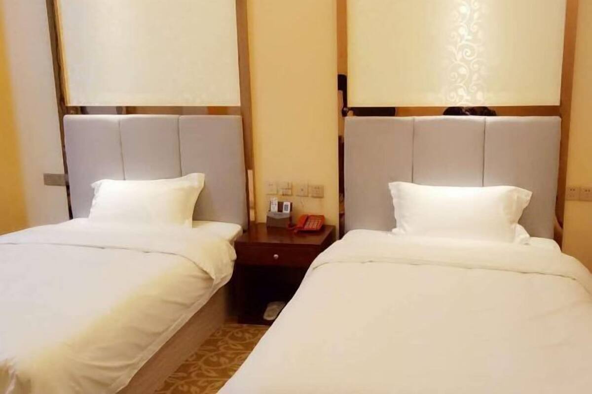 A hotel room with two single beds, each with a headboard and a bedside table.