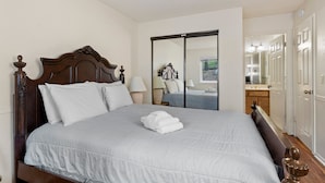 A neatly made bed with a wooden headboard, a bedside table with a lamp, and a sliding door leading to a bathroom. - Heavenly Chairview Condo 2 Bedroom Home by RedAwning (Stateline)