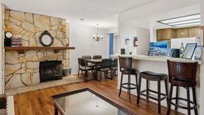 A living room with a stone fireplace, a dining area with a table and chairs, a bar area with stools, and a kitchen with wooden cabinets and a refrigerator. - Heavenly Chairview Condo 2 Bedroom Home by RedAwning (Stateline)