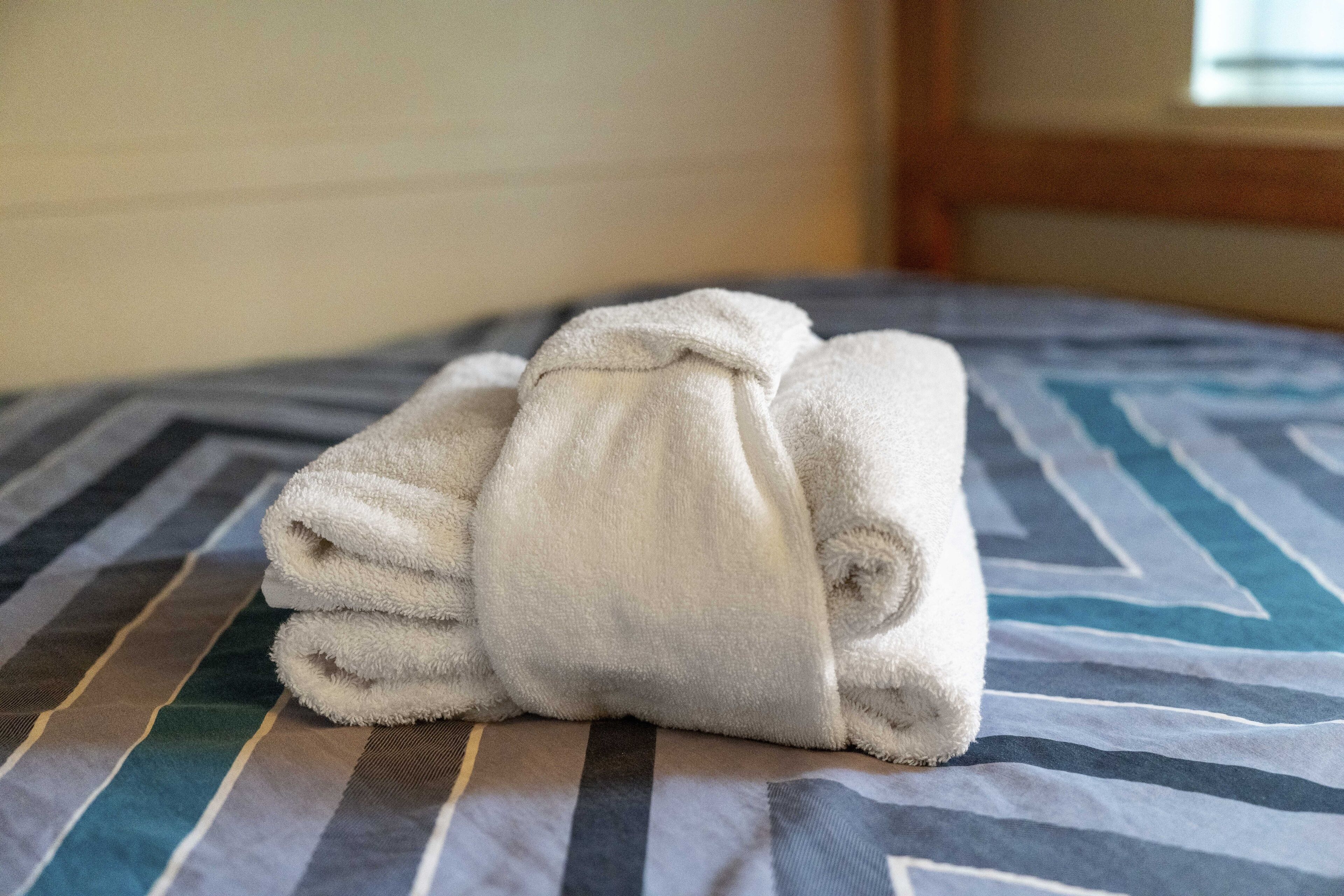 A neatly folded white towel on a bed with a striped bedspread.