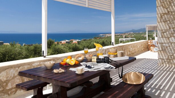 A wooden table set with breakfast items, a camera, and a view of the sea and landscape. - Two Bedroom Villa With Attic - Dalia (West Mani)
