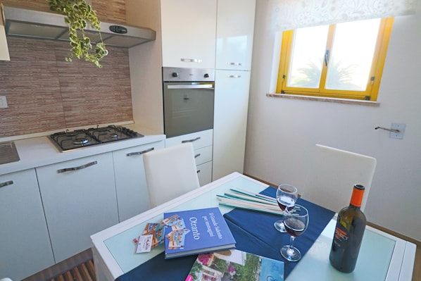 Une cuisine de taille réduite, équipée d’une cuisinière à gaz, d’un four et d’une fenêtre à cadre jaune.