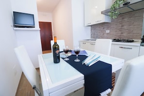 Une cuisine moderne avec un téléviseur fixé au mur, une table à manger avec une bouteille de vin et des verres, et une cuisinière à gaz.