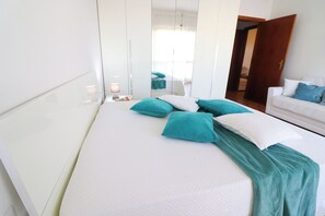 Quarto de hotel com uma cama, um sofá branco e um espelho.