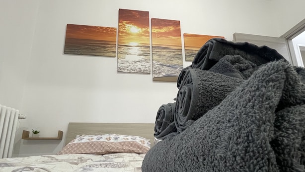 Una cama bien hecha con ropa de cama estampada, una planta en la mesita de noche y vista al mar a través de una ventana.