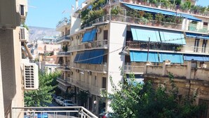 A balcony with a table and chairs, overlooking a street with parked cars and buildings. - Comfortable Apartment in Acropolis (Athens)