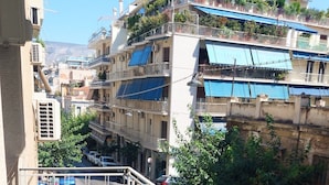 A balcony with a table and chairs, overlooking a street with parked cars and buildings.