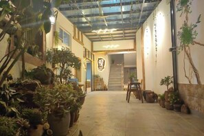 An indoor corridor with potted plants, a staircase, and a wooden bench. - Xingyue Courtyard-Style Hotel (Xiaojin)