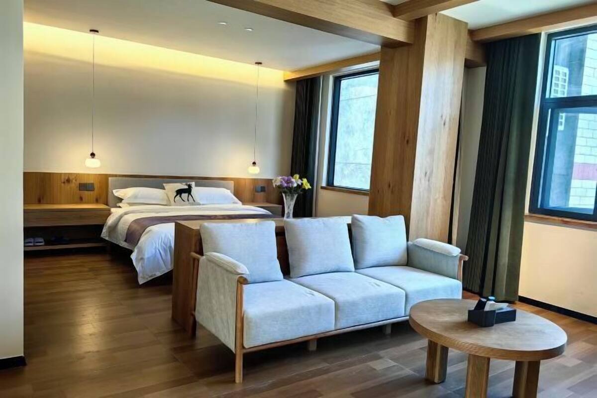 A modern hotel room with a wooden floor, a bed with white bedding, a light-colored sofa, and a round wooden table.