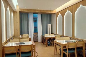 A dining area with tables and chairs, a view of the outside, and a large window with curtains. - Xingyue Courtyard-Style Hotel (Xiaojin)