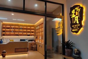A modern interior with a reception desk, shelves with items, and a neon sign. - Xingyue Courtyard-Style Hotel (Xiaojin)