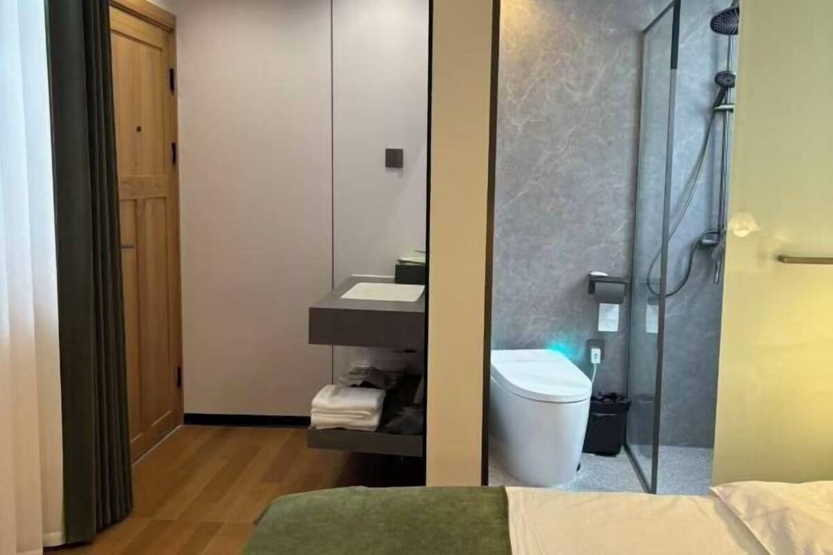 A hotel room with a bed, a bathroom with a shower, and a wooden wardrobe.