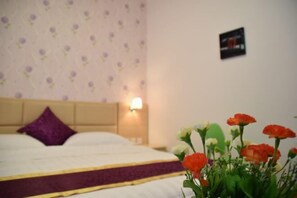 A hotel room with a bed, a purple pillow, a wall-mounted light, and a flower arrangement. - Xingyue Courtyard-Style Hotel (Xiaojin)