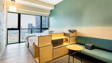 A modern hotel room with a large window, a bed, a sofa, and a small table.