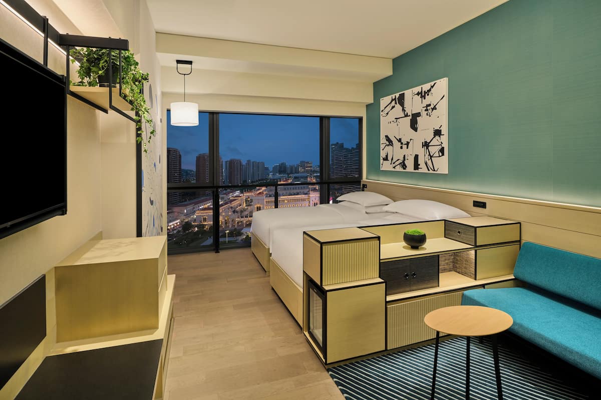 A modern hotel room with a large bed, a sofa, a small table, a TV, and a city view.