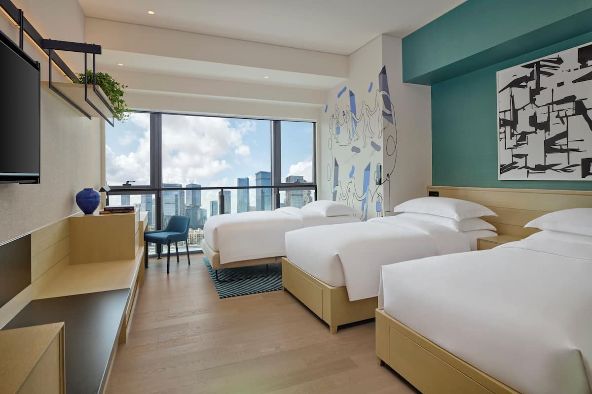 A hotel room with two beds, a desk, a chair, and a large window offering a city view.