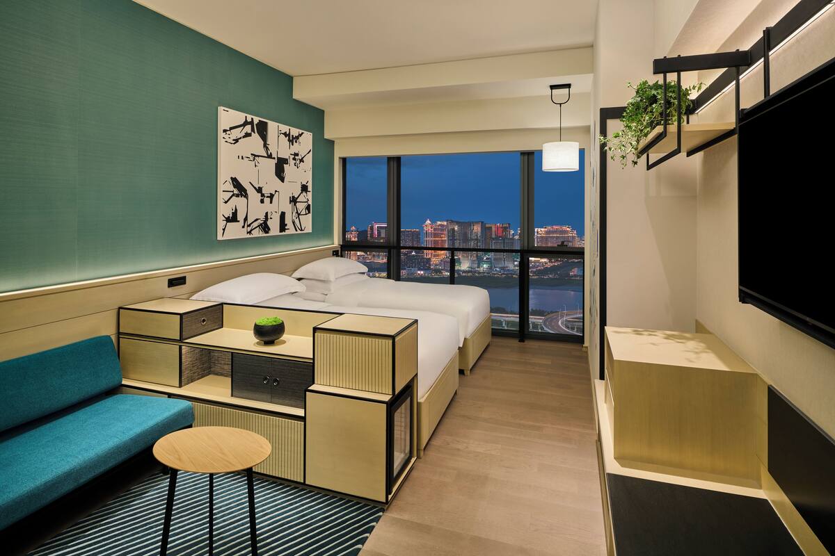 A modern hotel room with a large bed, a sofa, a small table, and a city view.