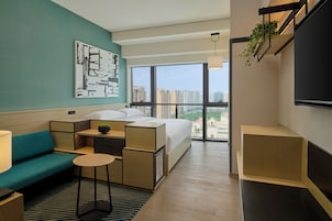 Una habitación de hotel moderna con una cama grande, un sofá, una mesita y un televisor.