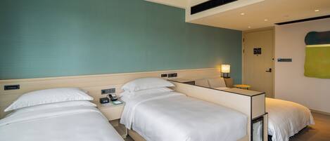 A hotel room with two beds, a bedside table with a lamp, and a small bedside table with a phone and a book.