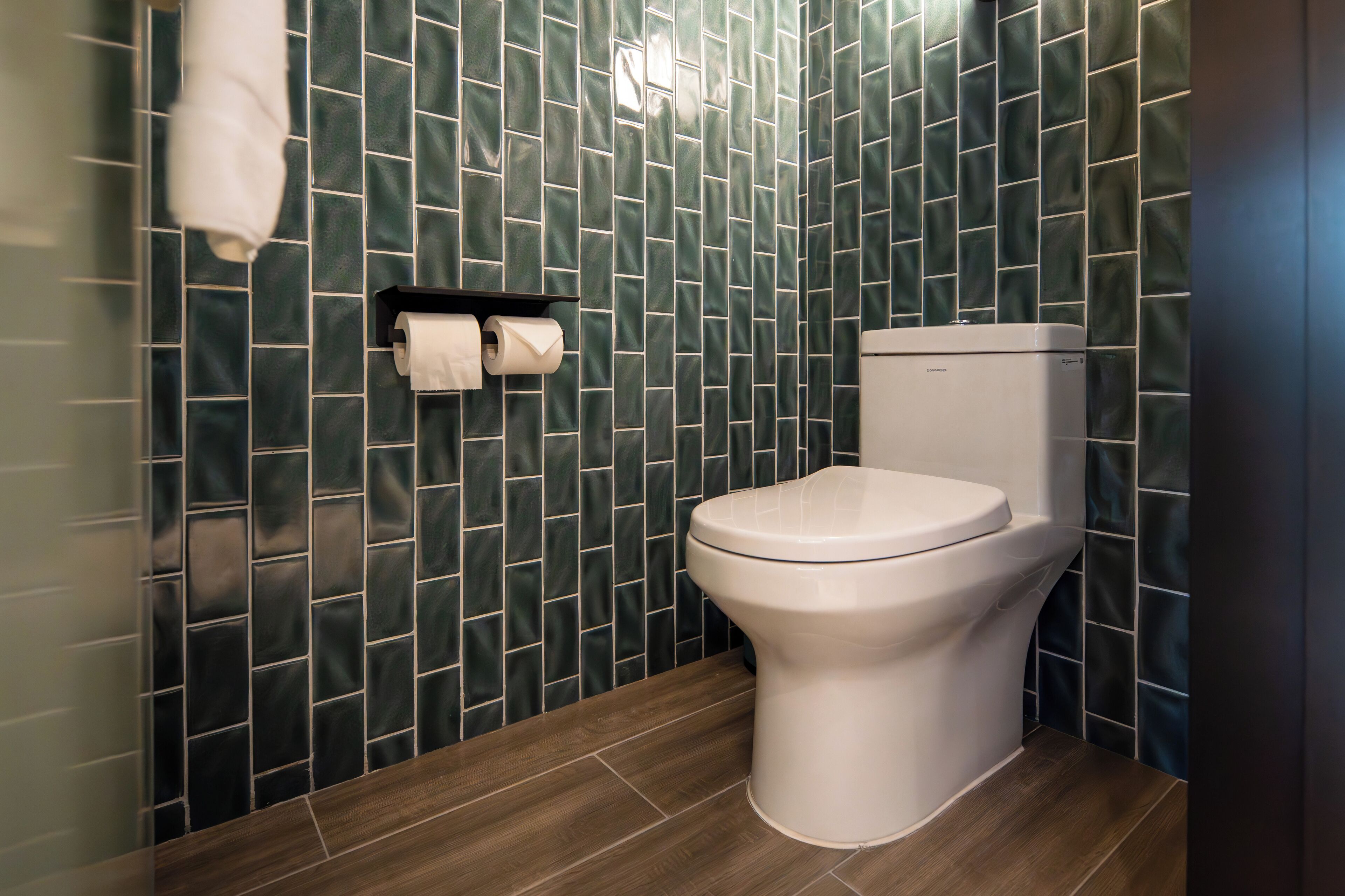 Een moderne badkamer met toilet, donkergroene betegelde wanden en een houten vloer.