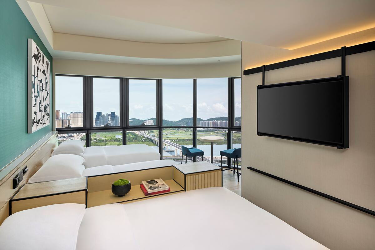 A modern hotel room with a large bed, a desk, and a seating area with a view of the city.
