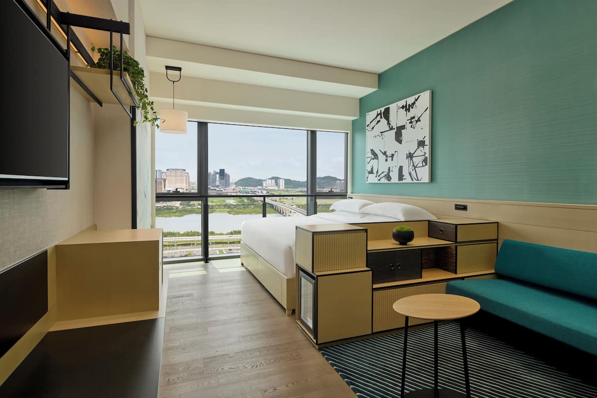 A modern hotel room with a large bed, a sofa, a small table, and a TV.