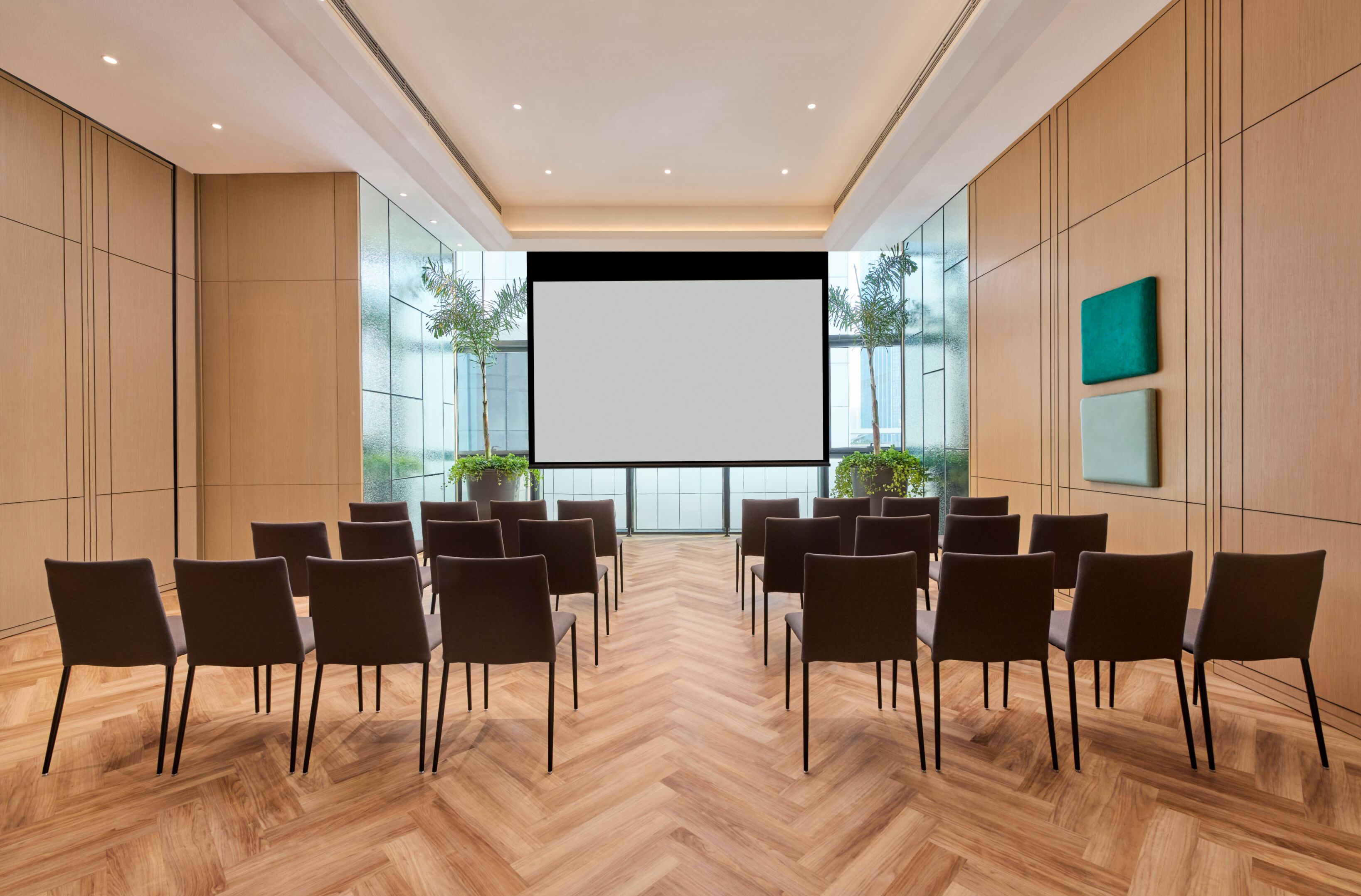 A conference room with a large screen, wooden panel walls, and a herringbone floor.