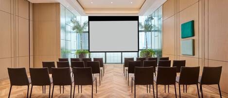 A conference room with a large screen, wooden panel walls, and a herringbone floor.