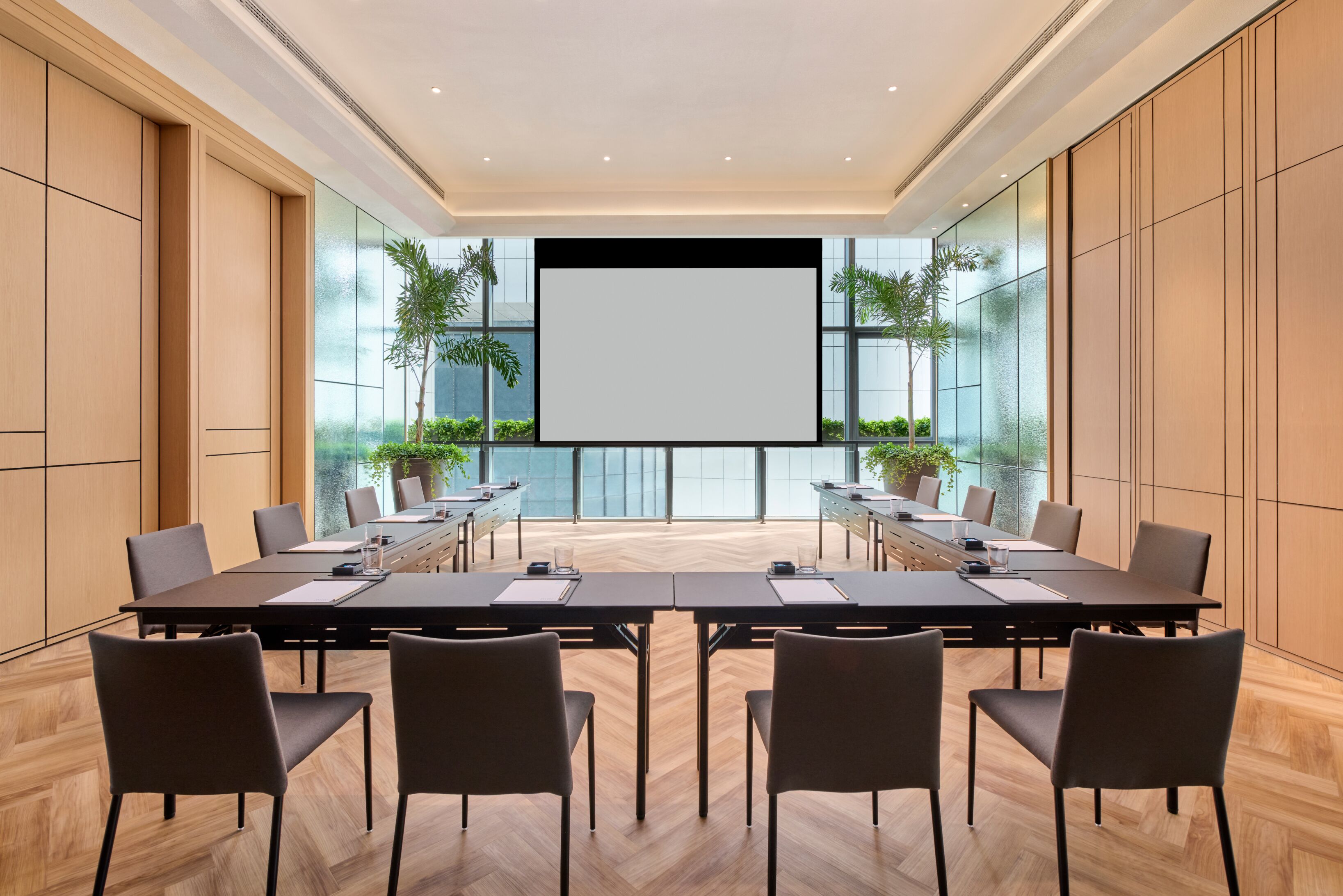 A conference room with a large table, chairs, a projector screen, and potted plants.