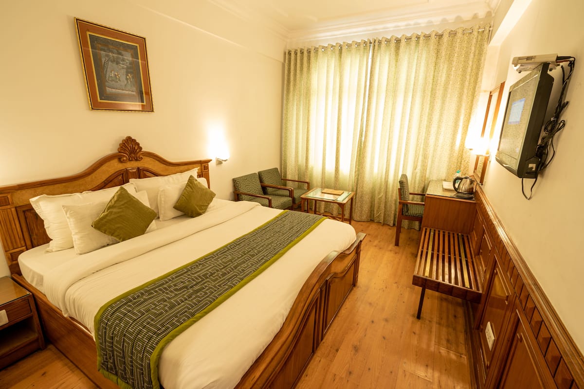 A hotel room with a large bed, a desk, a chair, and a television.