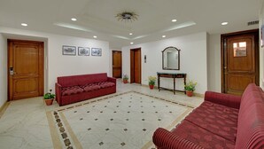 A hotel lobby with a red sofa, a wooden console table with a mirror, and a tiled floor. - Hotel Baljees Regency (Shimla)