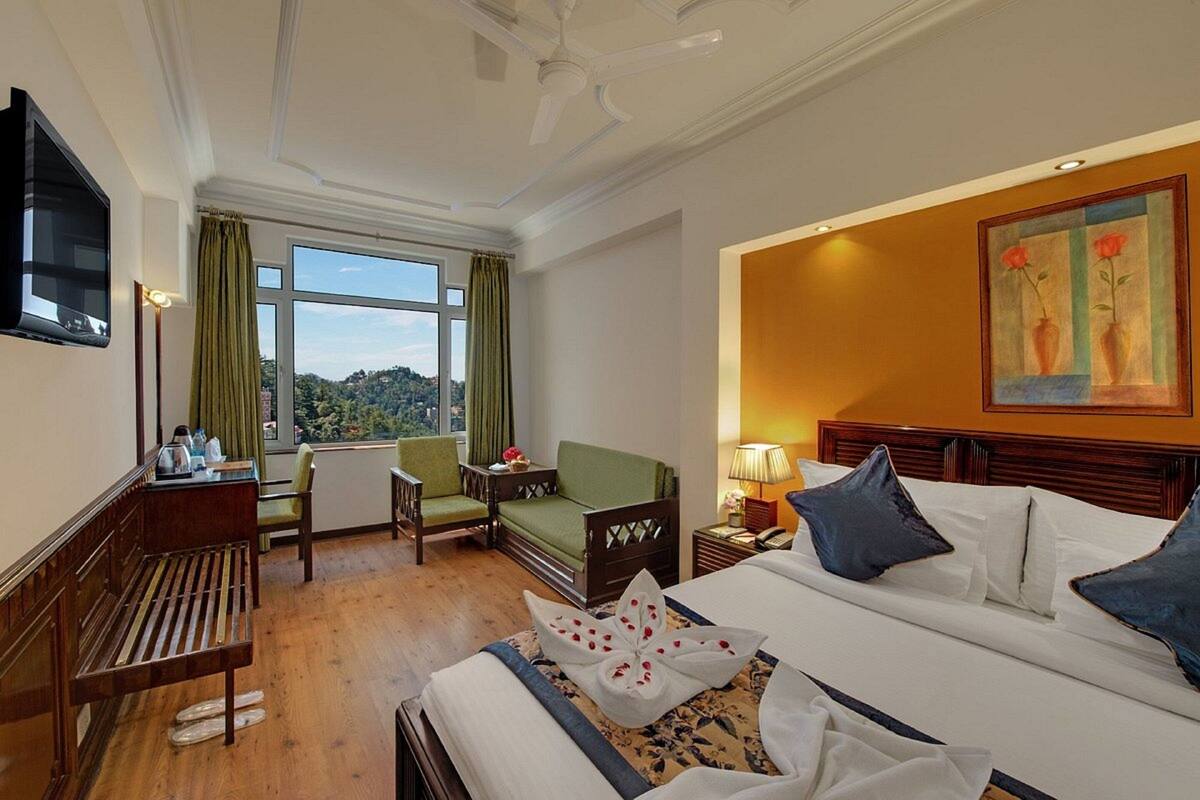 A hotel room with a bed, a desk with a chair, a sofa, a TV, and a window with a view.