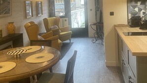 A modern kitchen with wooden cabinets, a dining area with a round table and chairs, and a view through a glass door to the outside. - Cozy is (Pont-Audemer)