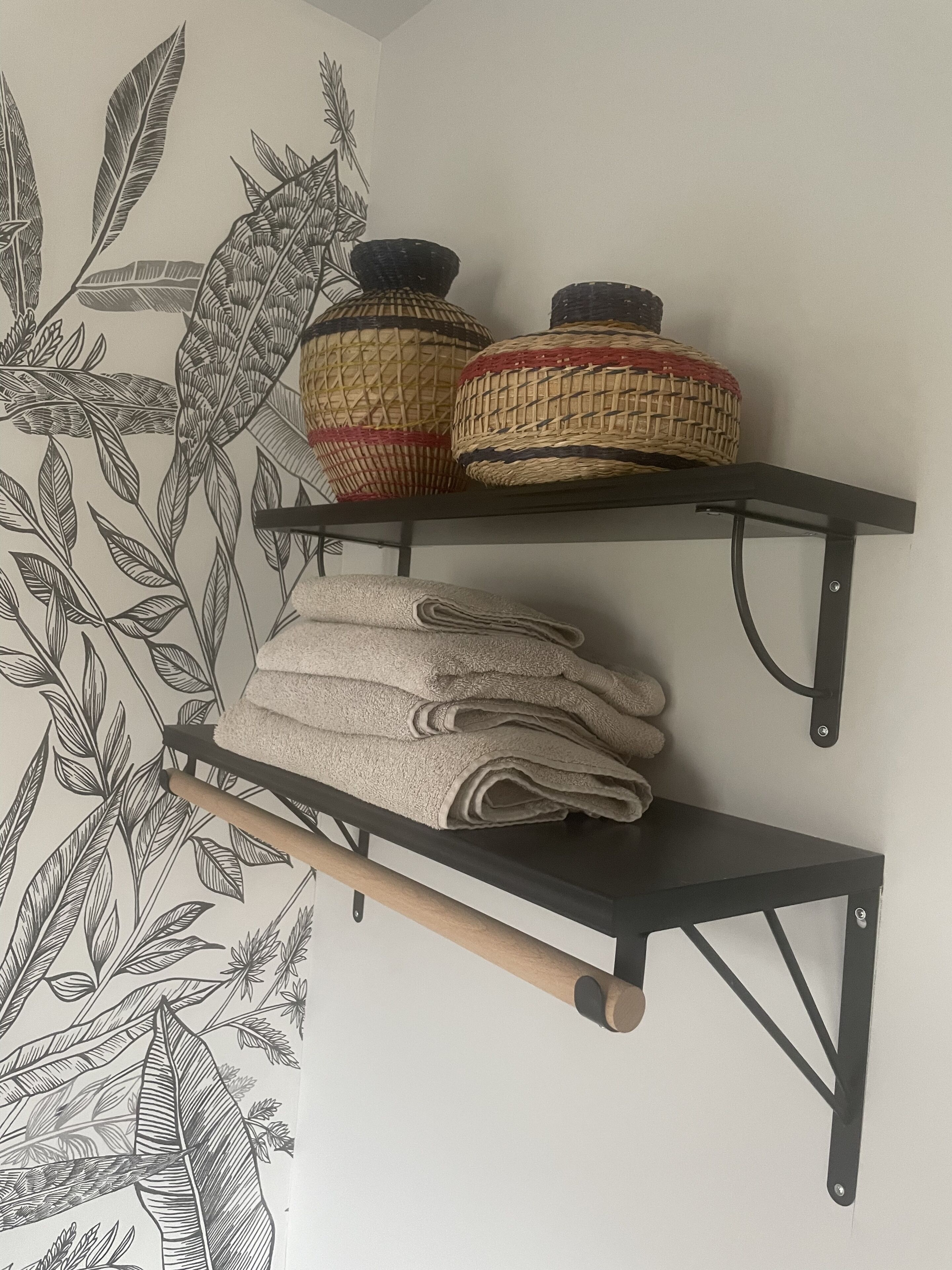 Een wand met een botanische print en twee planken met geweven manden en opgevouwen handdoeken.