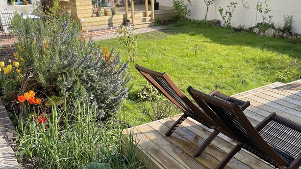 A backyard with a wooden deck, a bench, and a variety of plants and flowers. - Cozy is (Pont-Audemer)