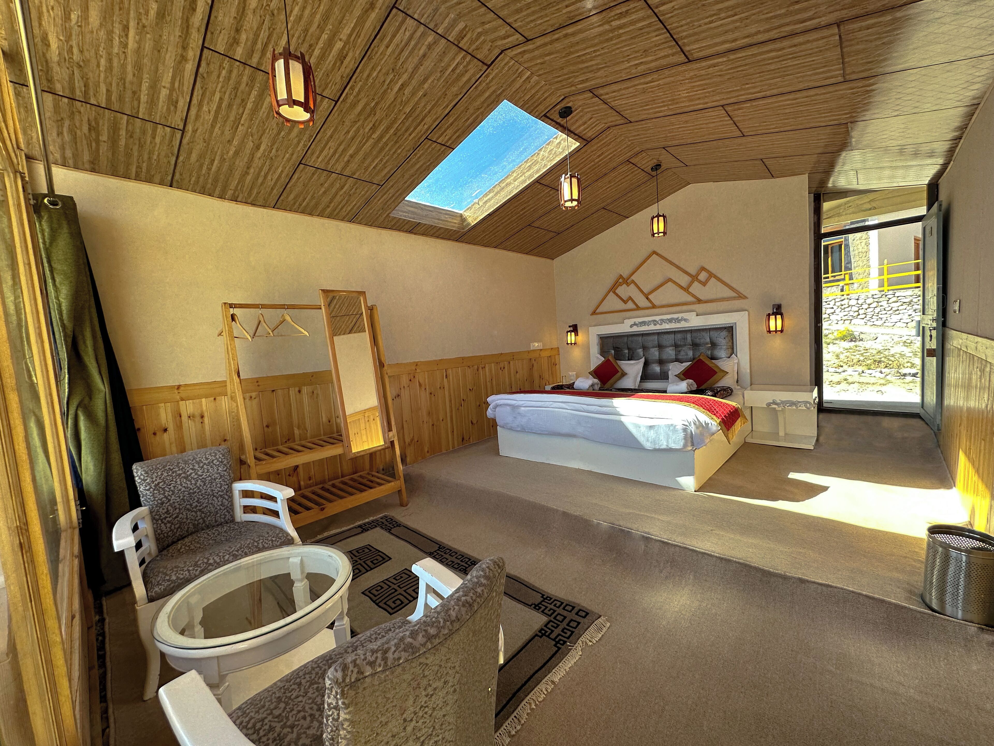 Quarto com cama, área de estar com cadeiras, mesa, espelho e vista para o exterior.