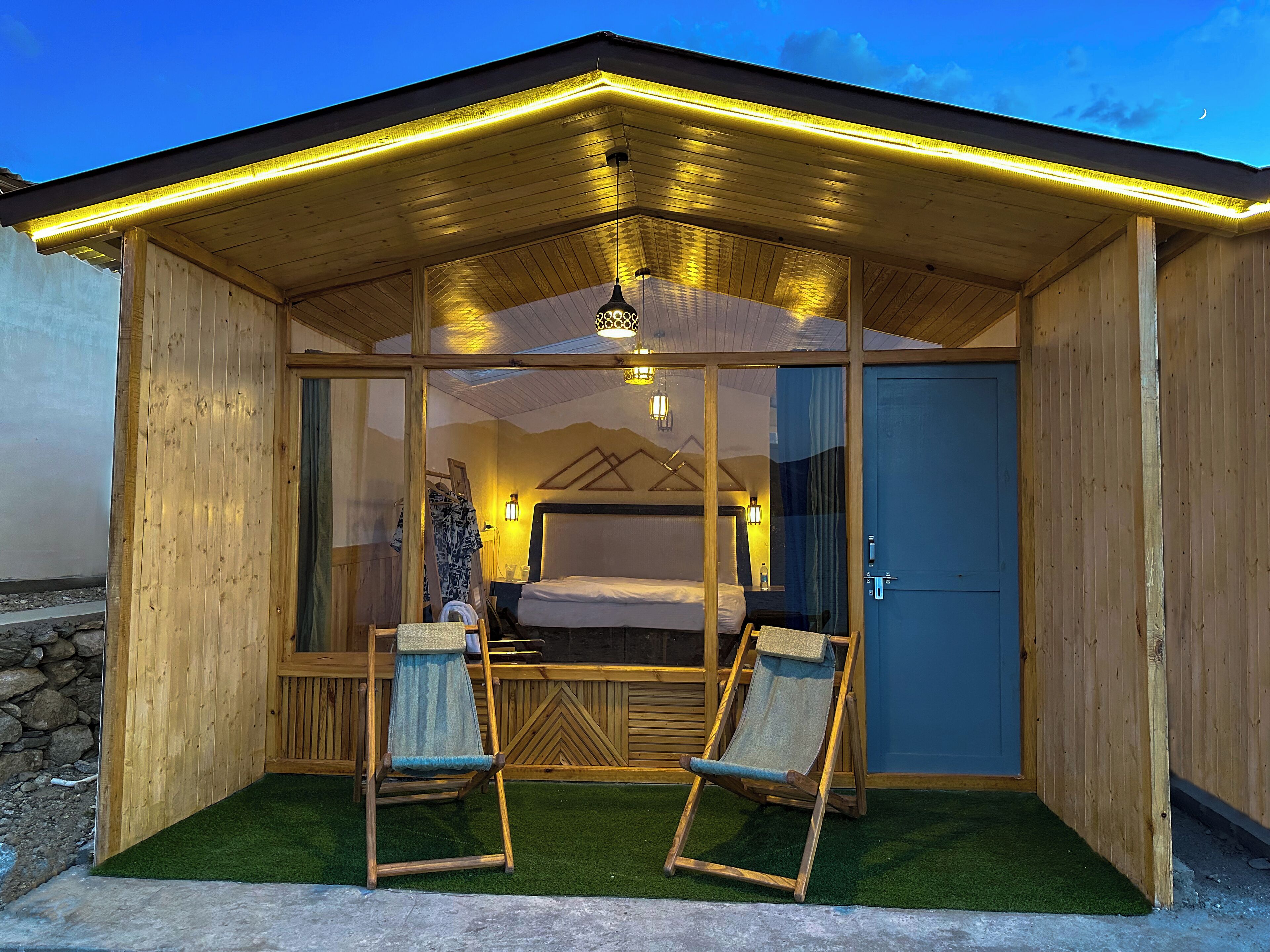 A wooden cabin with a glass-enclosed bedroom, two chairs, and a bed.