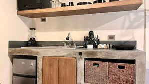 Uma cozinha compacta com geladeira embutida, micro-ondas e cafeteira em uma prateleira.