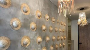 Corredor com parede decorada com vários chapéus, escada e luminária pendente.
