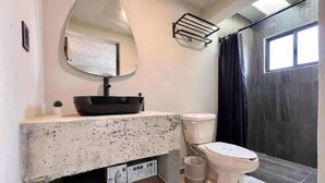 Ein Badezimmer mit fleckigem Waschtisch, einem großen Spiegel, einer Toilette und einer Duschkabine.