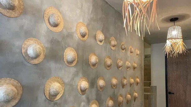 Ein Flur mit einer Wand, die mit vielen Strohhüten geschmückt ist, einer Holztür und einer Pendelleuchte.