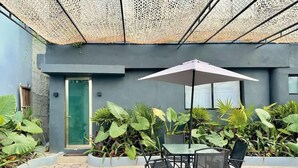 Eine Terrasse im Freien mit Tisch und Stühlen, umgeben von üppigem Grün und einer gemusterten Decke.