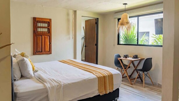 Une chambre à coucher avec un lit, une porte en bois, un coin repas avec des chaises et une table, et une fenêtre donnant sur un paysage agréable.